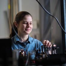 Crystal Senko photographed through black wires wearing a blue jean shirt working in a lab